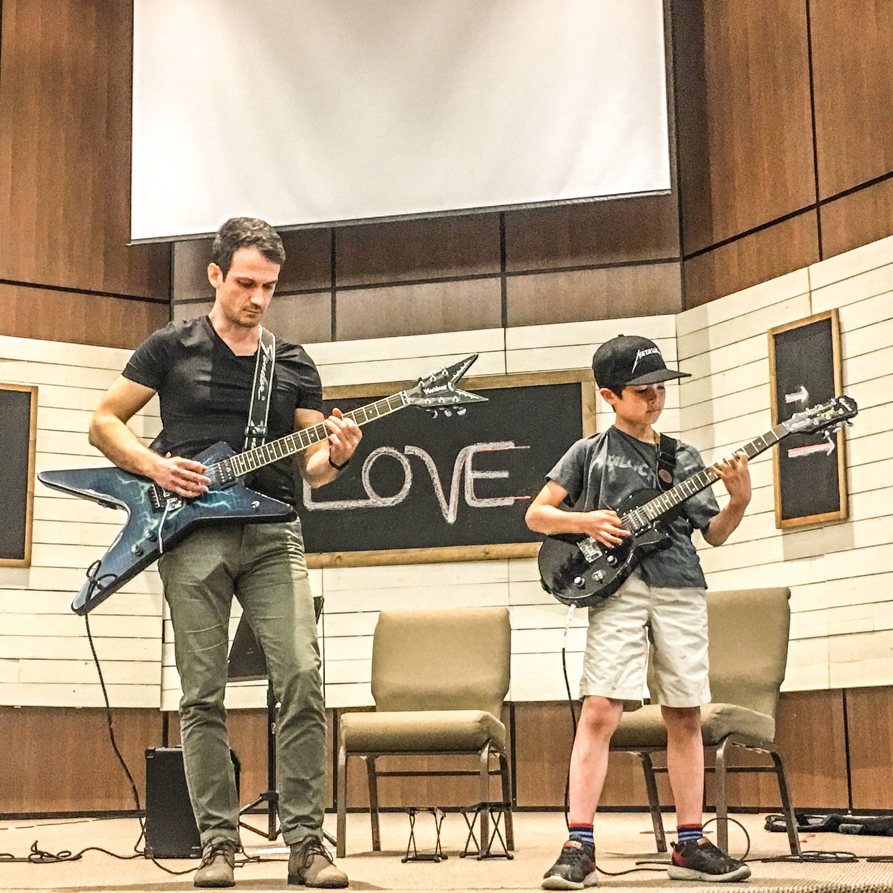 Julian Hasko and a young student playing electric guitars on stage at a recital